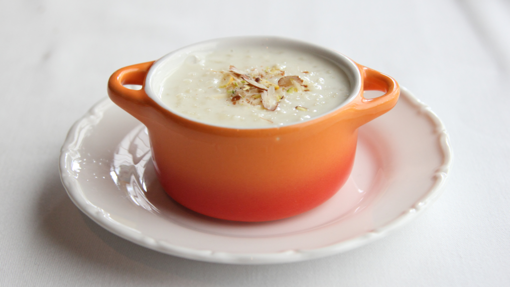 Traditional Palada Payasam served in an orange ceramic bowl, garnished with sliced almonds on a white plate.