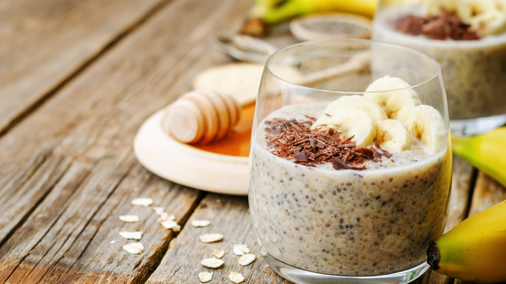 Glass of nutritious oats for weight loss with chia seeds, banana slices, and dark chocolate shavings, served with honey on a rustic wooden table.
