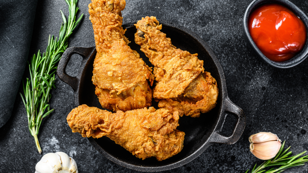 Crispy fried chicken drumsticks served in a cast-iron skillet with rosemary, garlic, and a side of ketchup.