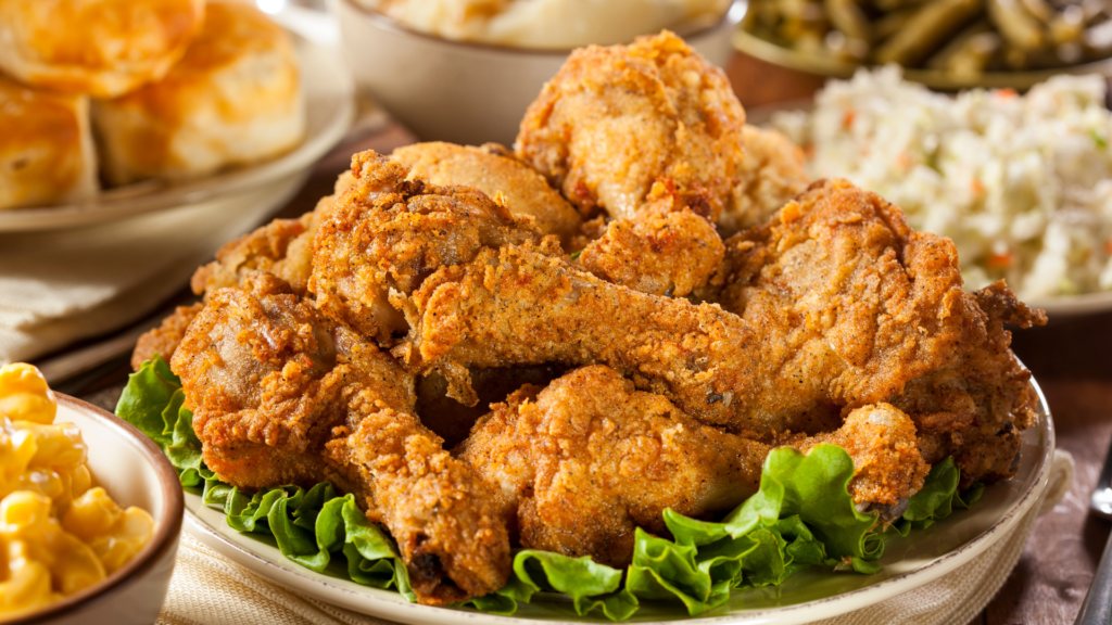 A plate of crispy fried chicken drumsticks served with mashed potatoes, coleslaw, biscuits, and macaroni and cheese.